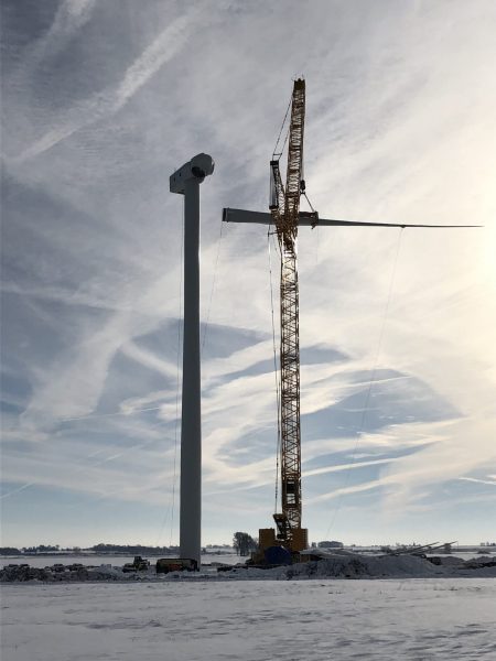 Installation team erecting a wind turbine at a wind farm site, supporting the development of renewable energy resources.