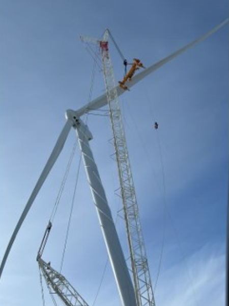 Workers assembling a wind turbine at a wind farm site, aiding in the advancement of renewable energy infrastructure.