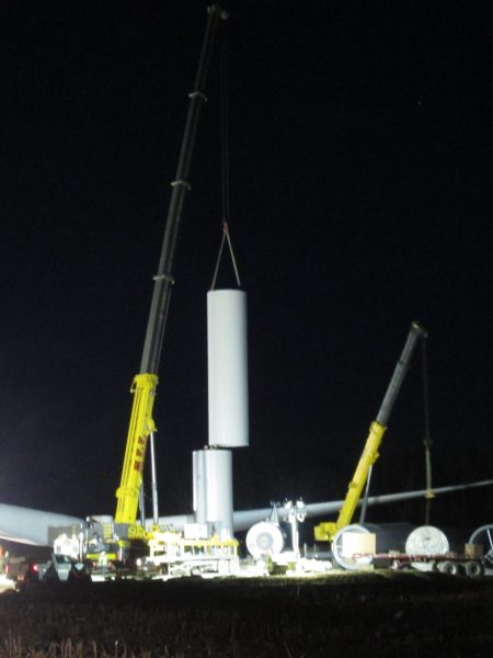 Night shift workers installing a wind turbine at a wind farm site, contributing to the growth of renewable energy infrastructure.
