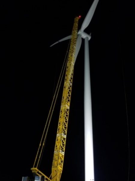 Workers installing a wind turbine at a wind farm site, contributing to the expansion of renewable energy production.