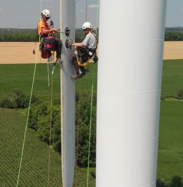 Rope access technicians performing maintenance and inspection services on a wind turbine tower at a wind farm.