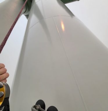 Worker conducting rope access services for cleaning and maintenance on a wind turbine tower, ensuring optimal performance and safety.